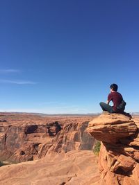 Woman sitting on rock against clear blue sky