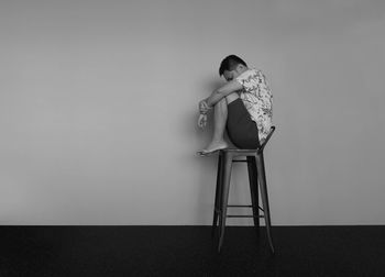 Woman sitting on chair against wall at home