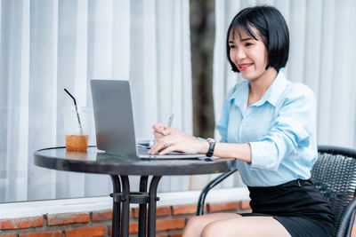 Young woman using mobile phone while sitting on table