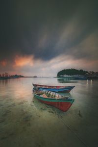 Boat moored at beach against sky during sunset