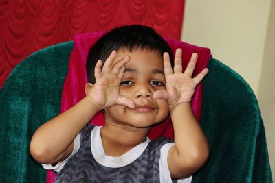 Portrait of boy gesturing while sitting on chair