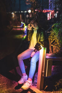 Portrait of young woman sitting by illuminated light at night