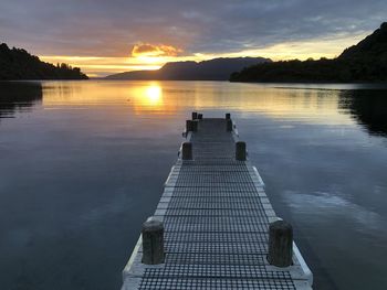 Pier on lake against sky during sunset