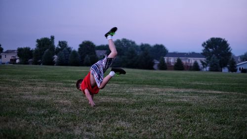 Full length of boy performing handstand on grassy field against sky