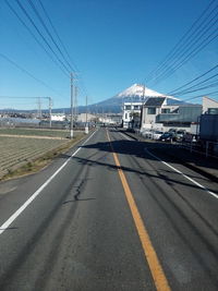 Road by electricity pylon in city against clear sky