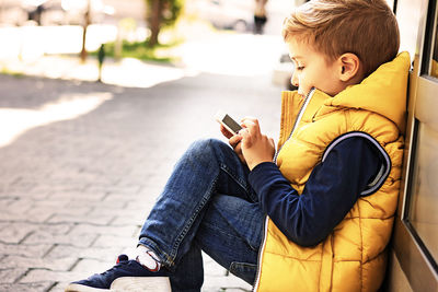 Rear view of boy sitting on mobile phone