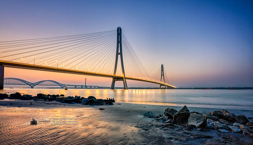 Suspension bridge over sea against sky during sunset