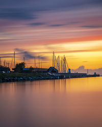 Sailboats moored in sea against sky during sunset