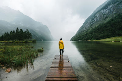 Rear view of man standing by lake against mountain