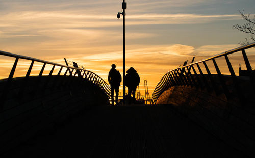 Rear view of silhouette people standing on footbridge against sky during sunset