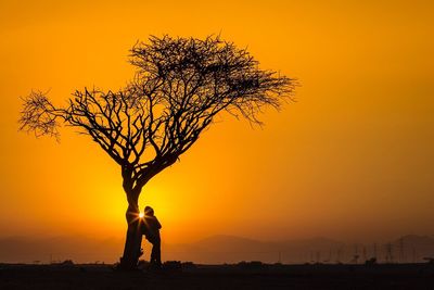 Silhouette man standing by tree against orange sky