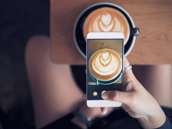 Close-up of hand holding coffee cup on table