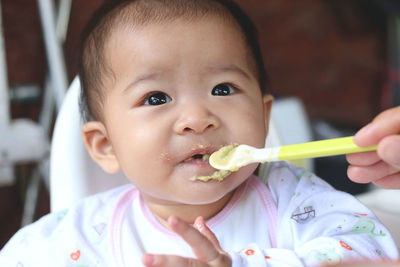 Cute baby girl eating food while looking away at home