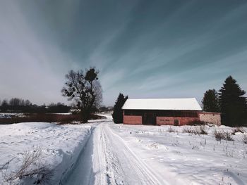 Snow covered field by building against sky