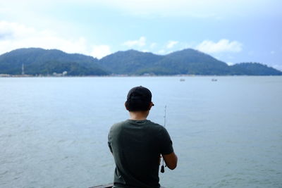 Rear view of young man fishing in sea against sky