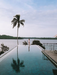 Side view of woman standing at edge of infinity pool against sky