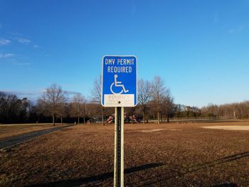 Road sign on field against clear blue sky