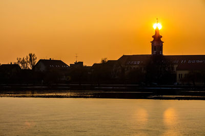 Illuminated city at waterfront during sunset