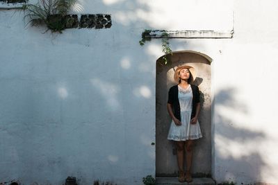 Portrait of young woman standing against wall