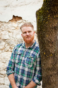 Portrait of man standing against tree trunk