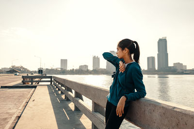 Side view of man sitting on bridge against sky