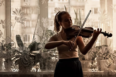Young woman playing violin by window