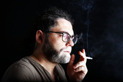 Portrait of man smoking cigarette against black background