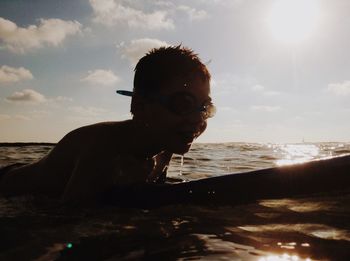 Close-up of boy sitting on beach against sky during sunset