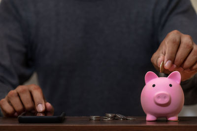 Midsection of man inserting coin in piggy bank