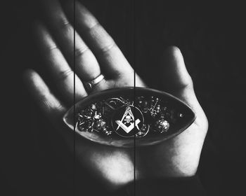 Close-up of hand holding clock against black background