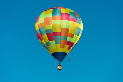 Low angle view of man and woman in hot air balloon against clear blue sky