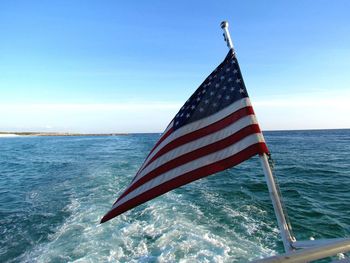 American flag on boat railing over sea against blue sky