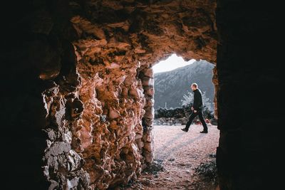 Man walking by rock formation seen through cave