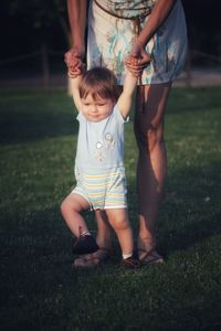 Midsection of mother and baby boy with blonde hair and blue eyes on grass making first steps