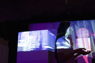 Side view of businesswoman gesturing by projection screen in illuminated convention center