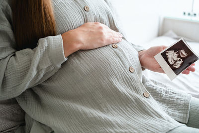 Midsection of pregnant woman looking at ultrasound photo 