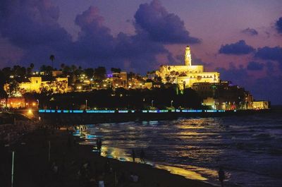 Illuminated buildings by river against sky at night