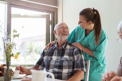 Senior man talking with female nurse while having breakfast in nursing home