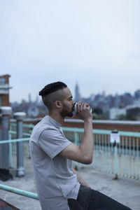 Man standing by railing against sky in city