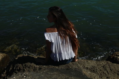 Rear view of young woman sitting on rock at seashore