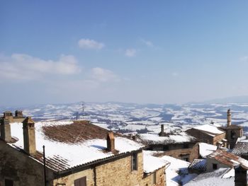 Snow covered houses by buildings against sky