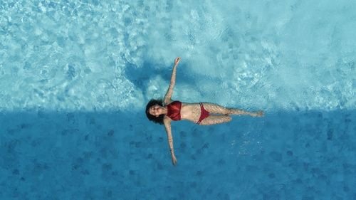 Woman in two peice swimming suit floating on blue swimming pool at the middle of light and shado