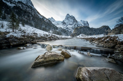 Scenic view of stream amidst snowcapped mountains against sky