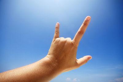 Low angle view of human hand gesturing horn sign against sky