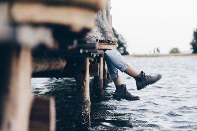 Low section of person sitting on pier over river against sky