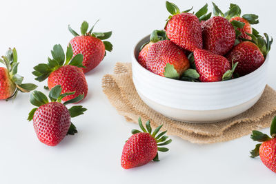 A bowl full of ripe strawberries with several scattered about on the table.