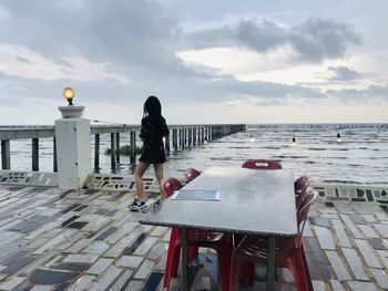 Rear view of woman standing by railing against sea