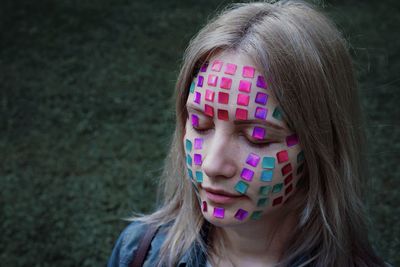 Close-up of woman with colorful crystals on face against wall