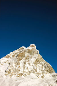 Low angle view of snowcapped mountain against clear blue sky