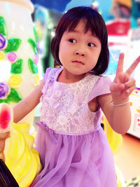 Cute girl showing peace sign while sitting at amusement park ride